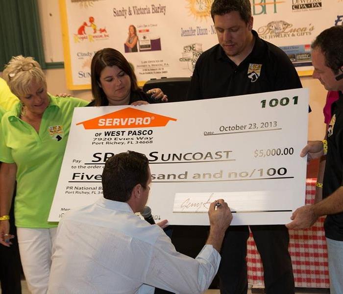two women and a man holding a large check and a man in white shirt signing it